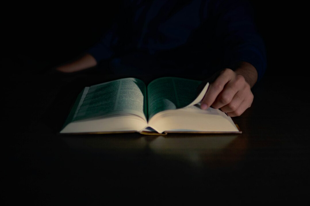 Hands of a person turning the pages of a book under a warm reading lamp at night